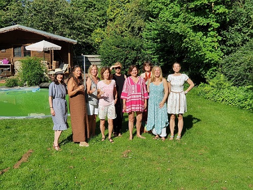 Hier stehen 10 Frauen auf einer Wiese im Sonnenschein und lachen in die Kamera