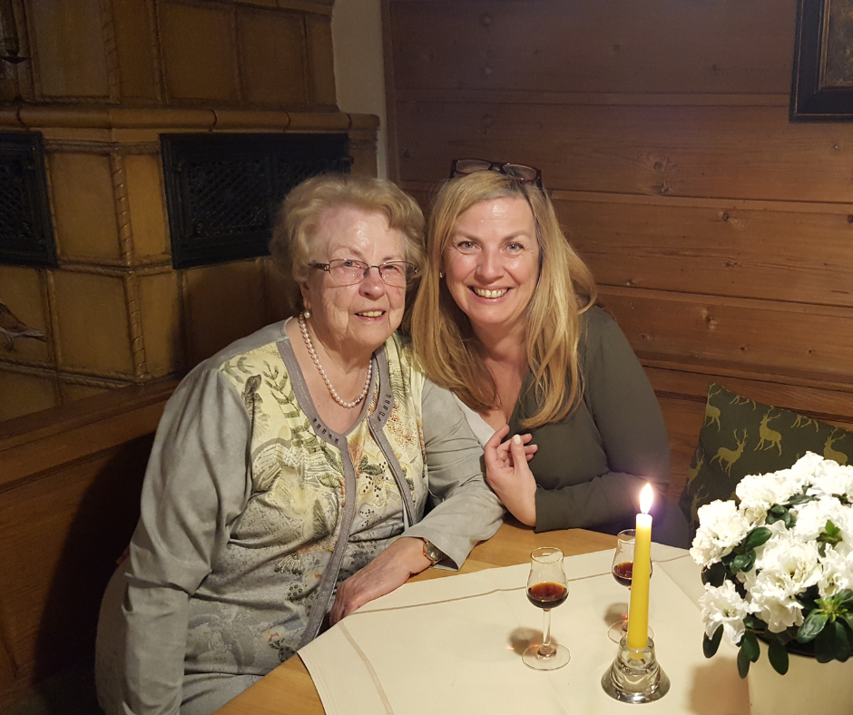 Mutter und Tochter in einer gemütlichen Wirtsstube sitzen beieinander bei einem Gläschen Likör. Eine Kerze brennt auf dem Tisch.